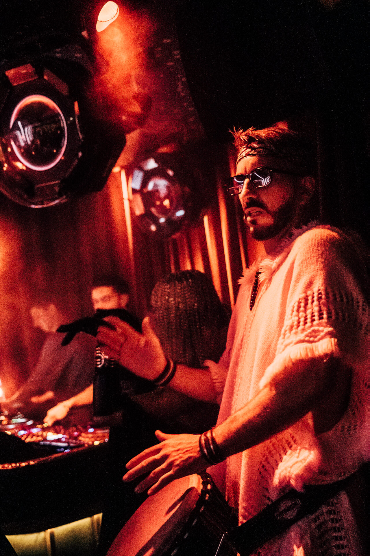 Selva Monte Carlo DJ performing live during a night out, surrounded by atmospheric red lighting and a lively nightclub crowd.